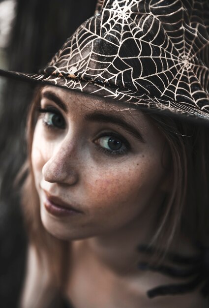 Mujer atractiva con sombrero de telaraña decorativa mirando a cámara