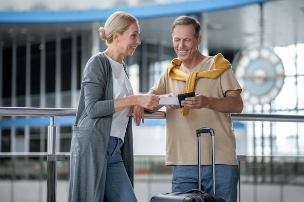 Mujer atractiva sonriente hablando con un hombre alegre y guapo con el boleto de embarque y un pasaporte extranjero