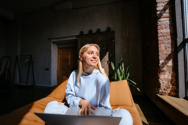 Mujer atractiva sonriente que miente en cama usando la computadora portátil