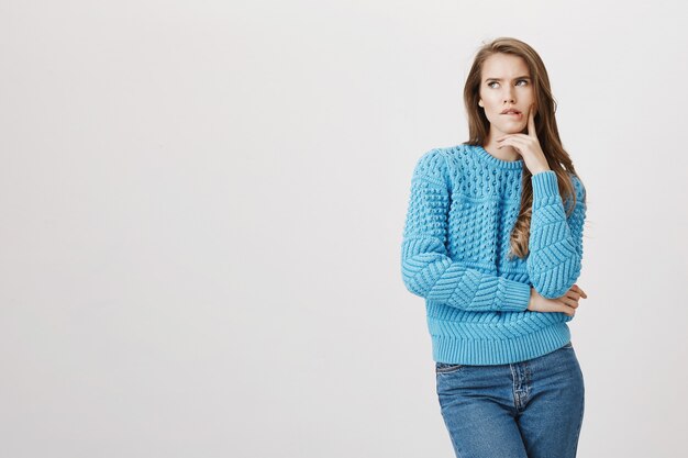 Mujer atractiva en suéter pensando, mordiendo el labio pensativo