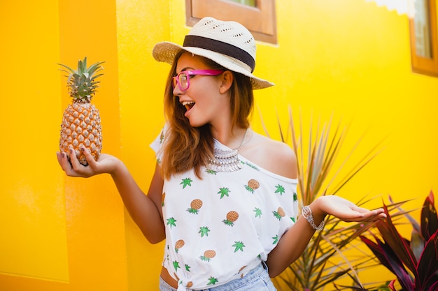 Mujer atractiva en vacaciones de verano con expresión de la cara divertida sonriente emocional vistiendo sombrero de paja sentado descalzo sorprendido