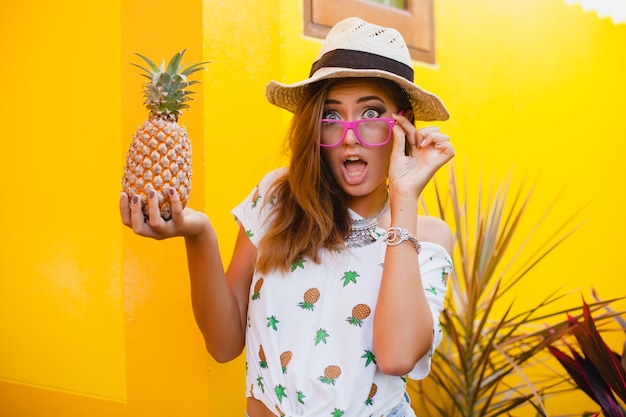 Mujer atractiva en vacaciones de verano con expresión de la cara divertida sonriente emocional vistiendo sombrero de paja sentado descalzo sorprendido