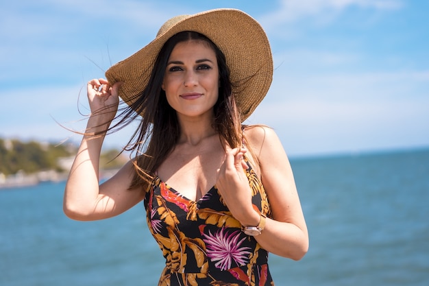 Mujer atractiva con un vestido de flores y un sombrero capturado por el hermoso mar en España