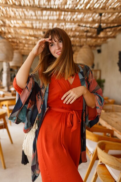 Mujer atractiva en vestido de moda naranja posinng en café tropical. Traje brillante. Concepto de moda de viajes y vacaciones.