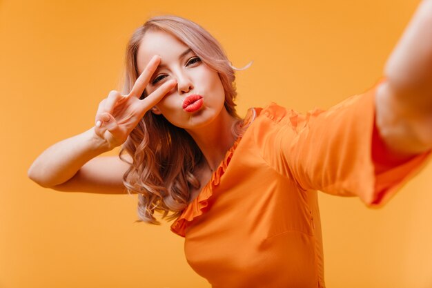 Mujer atractiva en vestido naranja haciendo selfie