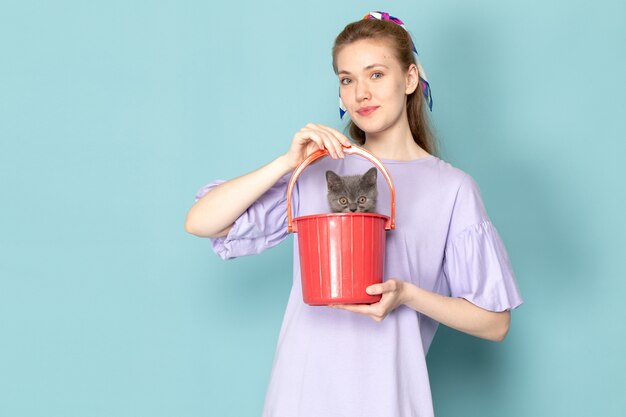 Una mujer atractiva de la vista frontal en camisa púrpura que sostiene el cubo rojo con el gatito lindo en azul