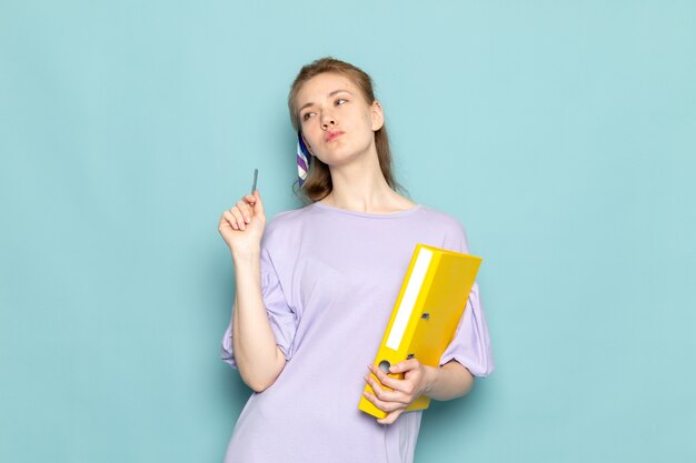 Una mujer atractiva de vista frontal en camisa-vestido azul con archivos amarillos sobre fondo azul trabajo de negocios de ropa de dama