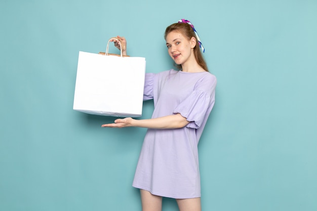 Una mujer atractiva de la vista frontal en camisa-vestido azul que sostiene el paquete de compras blanco en azul