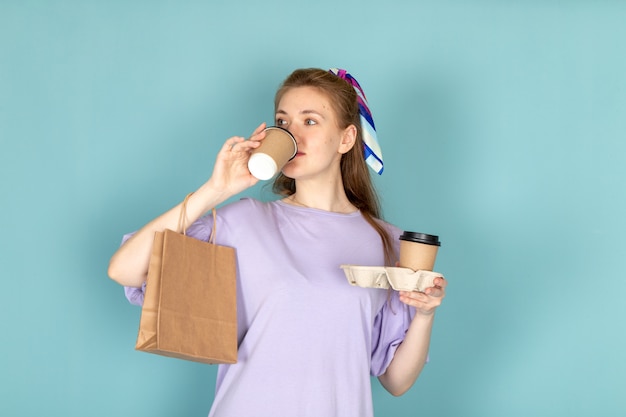 Una mujer atractiva de vista frontal en camisa-vestido azul sosteniendo el paquete de papel y tazas de café bebiendo en azul