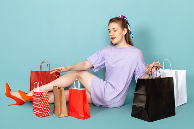 Una mujer atractiva de vista frontal en camisa-vestido azul sosteniendo paquetes de compras y sentado en azul