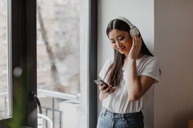 mujer en auriculares blancos se encuentra cerca de la ventana