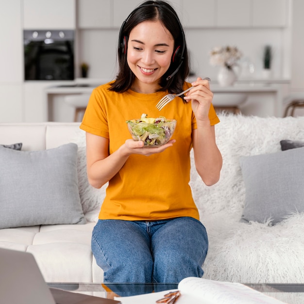 Foto gratuita mujer con auriculares comiendo mientras asiste a una videollamada