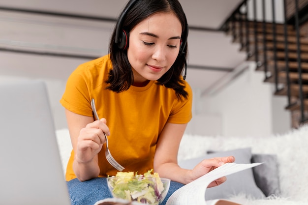 Mujer con auriculares comiendo mientras asiste a una videollamada