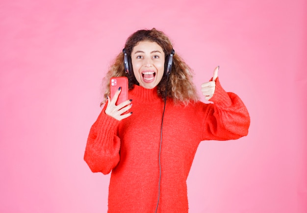 mujer con auriculares escuchando su lista de reproducción en el teléfono inteligente y mostrando el signo de disfrute.