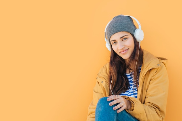 Foto gratuita mujer con auriculares mirando a la cámara sentado frente a fondo amarillo liso