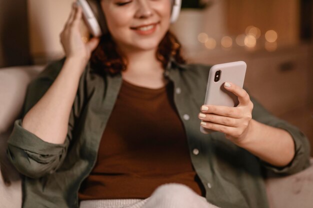 Mujer con auriculares modernos y dispositivo de teléfono inteligente en casa en el sofá