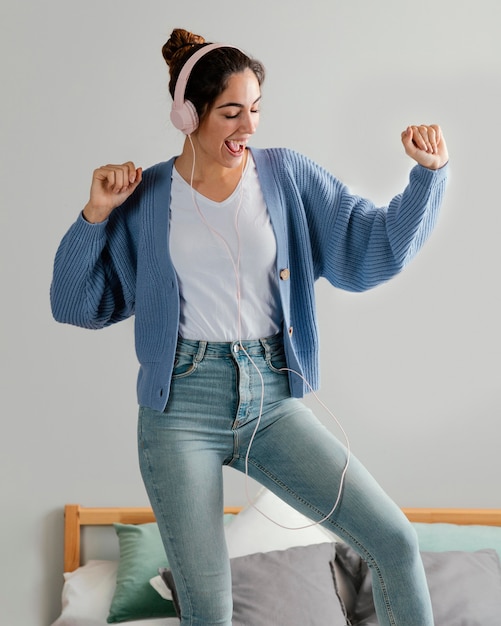 Mujer con auriculares para música en casa y bailando en la cama