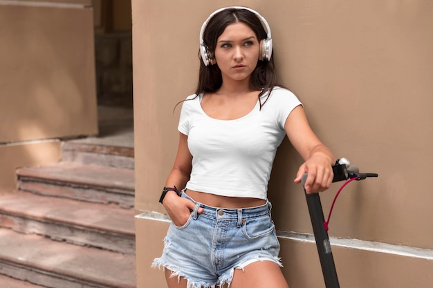 Mujer con auriculares posando junto a scooter eléctrico