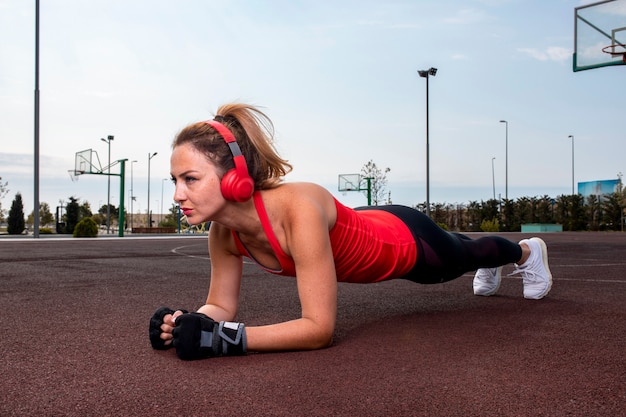 Mujer con auriculares rojos haciendo ejercicios abdominales en la tierra en el parque.