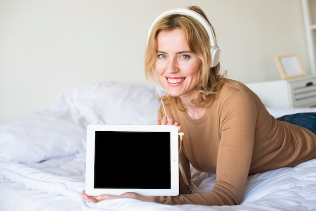Mujer en auriculares sosteniendo tablet con pantalla en blanco