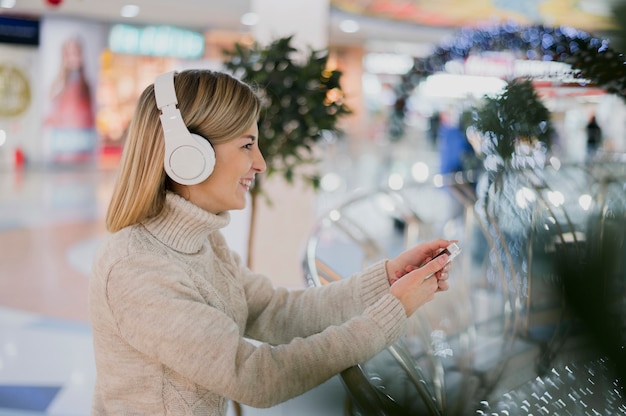 Mujer con auriculares y sosteniendo el teléfono en el centro comercial