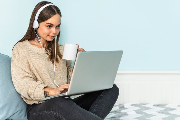 Mujer con auriculares usando laptop y tomando café en casa durante la pandemia