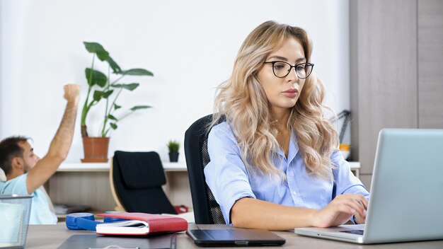 Mujer autónoma que trabaja en la computadora portátil en la casa mientras el esposo está viendo la televisión en el fondo