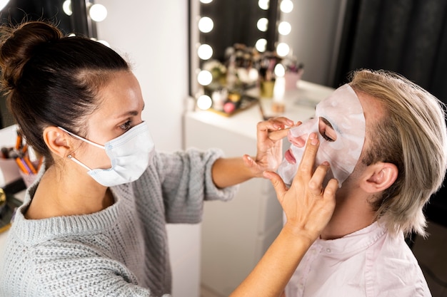 Mujer ayudando al hombre aplicando una mascarilla facial