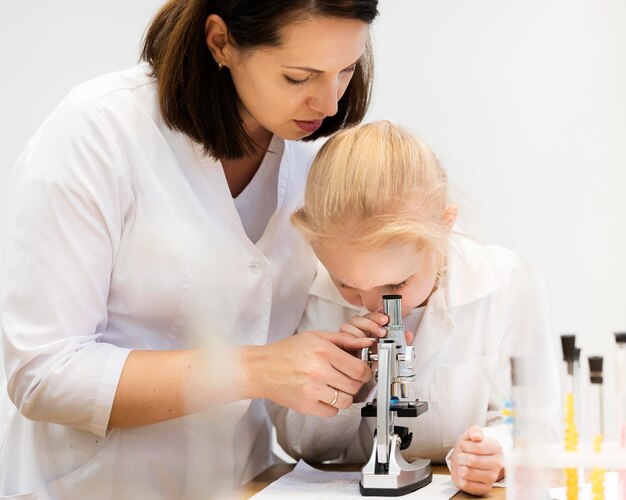 Mujer ayudando a niña a usar microscopio