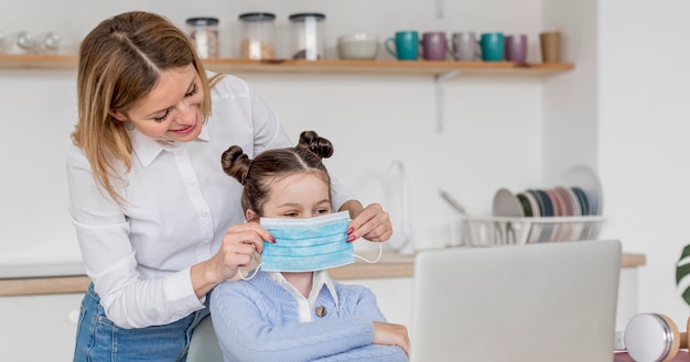 Foto gratuita mujer ayudando a su hija a ponerse una máscara médica