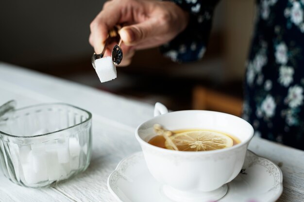 Mujer ayudándose con un cubo de azúcar para su taza de té de limón caliente agradable
