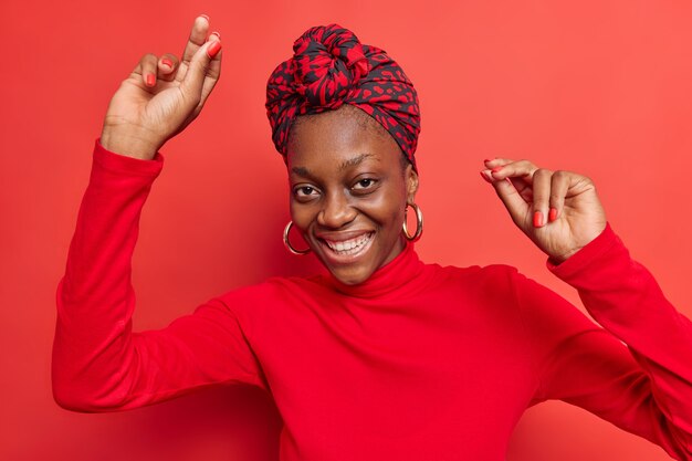 mujer baila sola levanta los brazos y se mueve sonríe agradablemente vestida se siente optimista celebra los buenos resultados del trabajo vestida con ropa elegante aislada en rojo