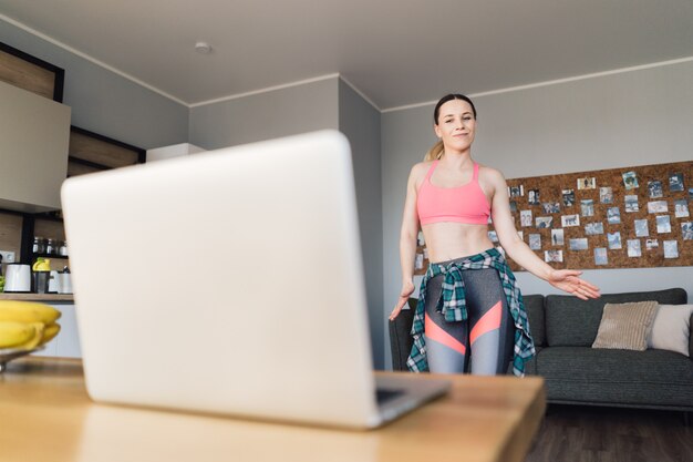 Mujer bailando en casa siguiendo lecciones en video en la computadora portátil