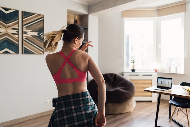 Mujer bailando en casa siguiendo lecciones en video en la computadora portátil