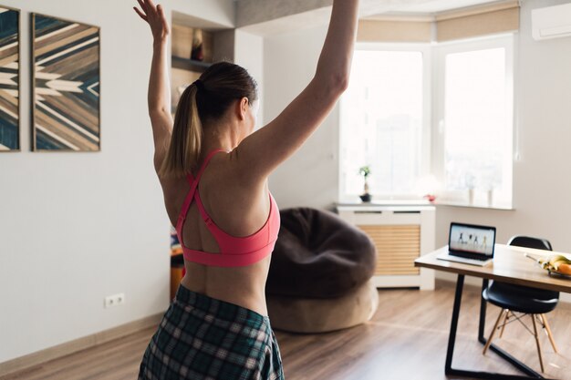 Mujer bailando en casa siguiendo lecciones en video en la computadora portátil