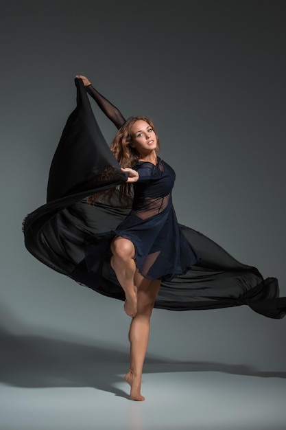 Foto gratuita mujer bailarina con un vestido negro. danza moderna contemporánea sobre un fondo gris. fitness, modelo de estiramiento