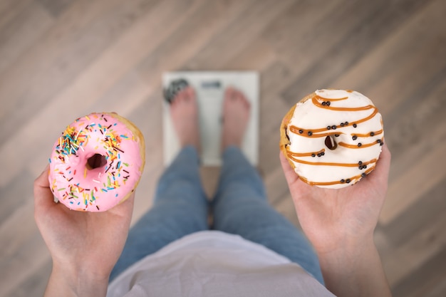 Una mujer se para en la balanza sostiene donas en su espacio de copia de la vista superior de las manos