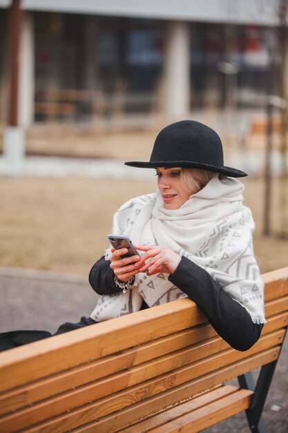 Foto gratuita mujer en banco escribiendo en el smartphone