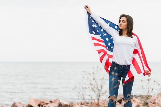 Mujer con bandera americana por el mar