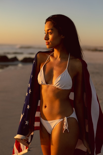 Mujer con una bandera americana de pie en la playa