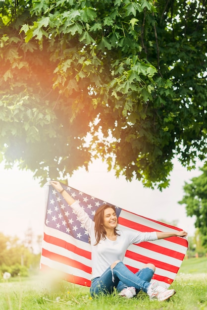 Foto gratuita mujer con bandera americana sentada debajo de árbol