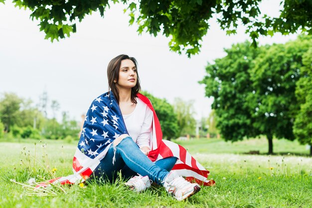 Mujer con bandera americana sentada debajo de árbol