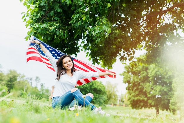 Mujer con bandera americana sentada debajo de árbol