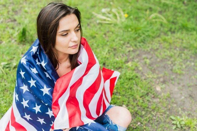 Mujer con bandera americana sentada en la naturaleza
