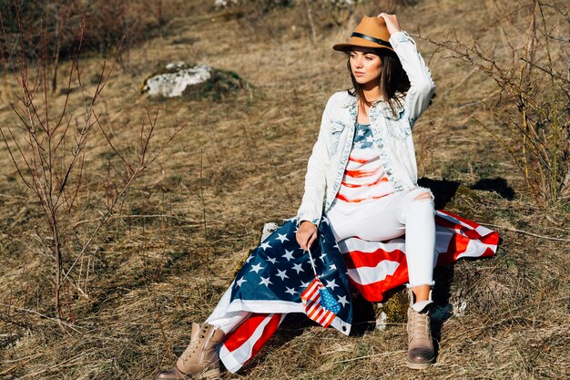 Mujer con bandera americana sentada en la naturaleza