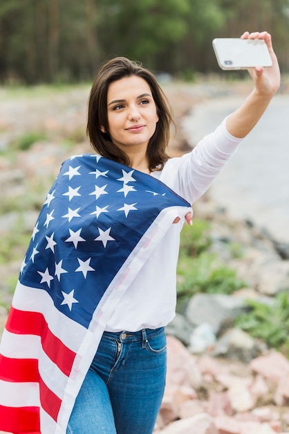 Foto gratuita mujer con bandera americana tomando selfie en la naturaleza