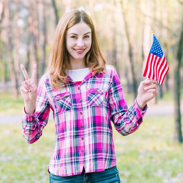 Mujer con bandera de los Estados Unidos mostrando el signo de la victoria