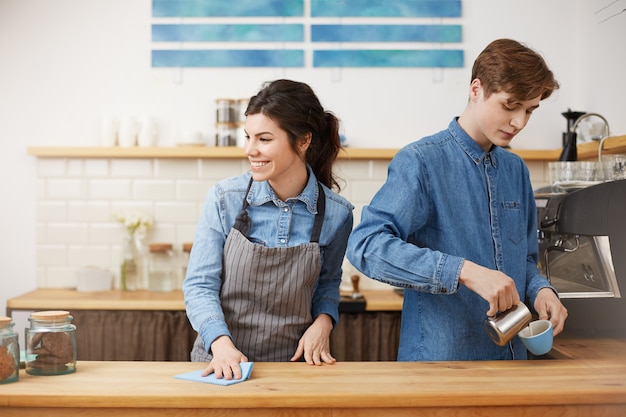 Mujer barista esponja abajo de la mesa sonriendo felizmente. Prepara café vertido.