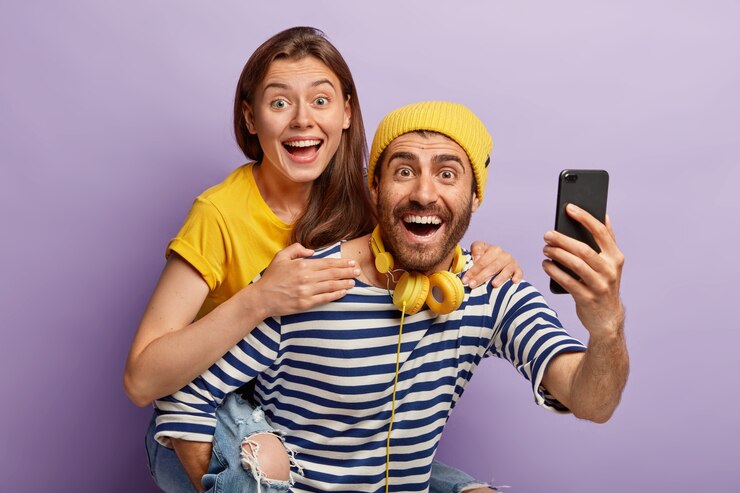 Foto gratuito mujer bastante alegre cabalga sobre la espalda de su novio, toma selfie, tiene expresiones alegres