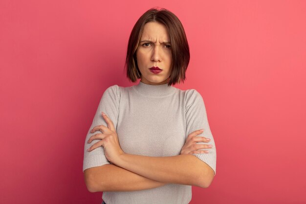 Mujer bastante caucásica molesta se encuentra con los brazos cruzados en rosa